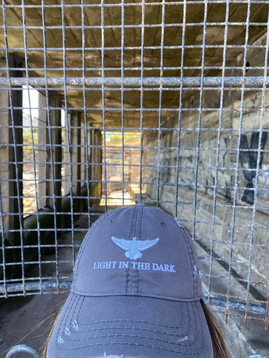 Grey distressed cap with "LIGHT IN THE DARK" embroidered on the front and a white dove above, symbolizing hope in dark moments