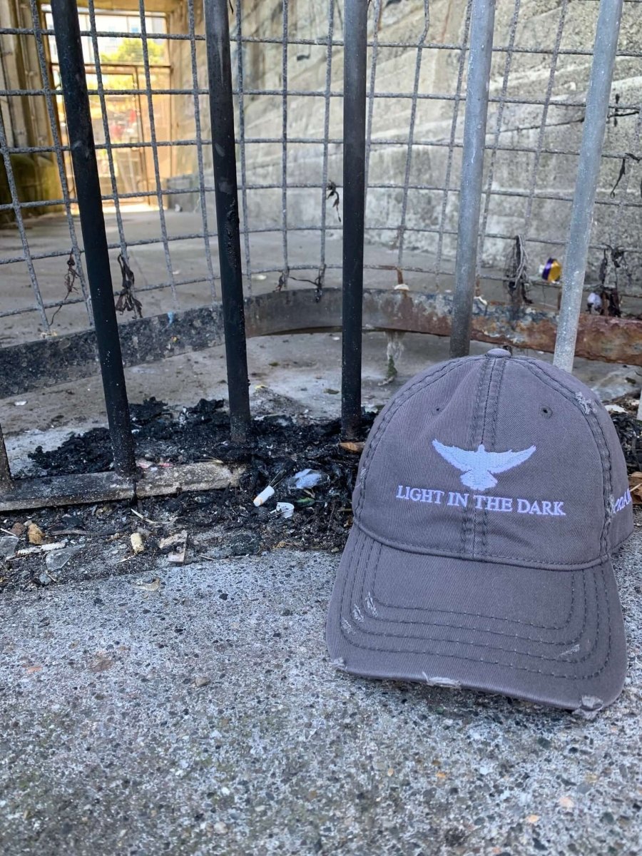 Grey distressed cap with "LIGHT IN THE DARK" embroidered on the front and a white dove above, symbolizing hope in dark moments.