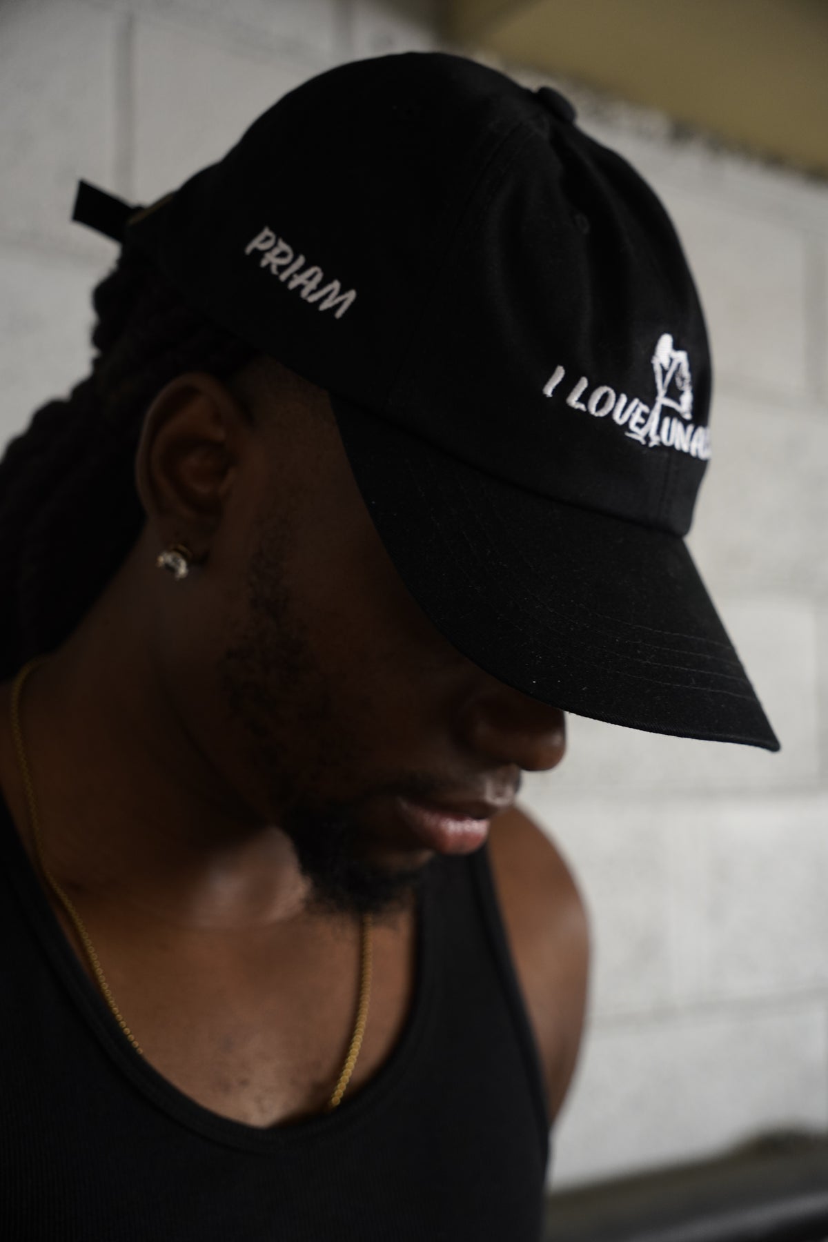 A man wearing a black baseball cap with white embroidered text reading 'PRIAM' and 'I LOVE ANIMALS' on a white brick wall background.